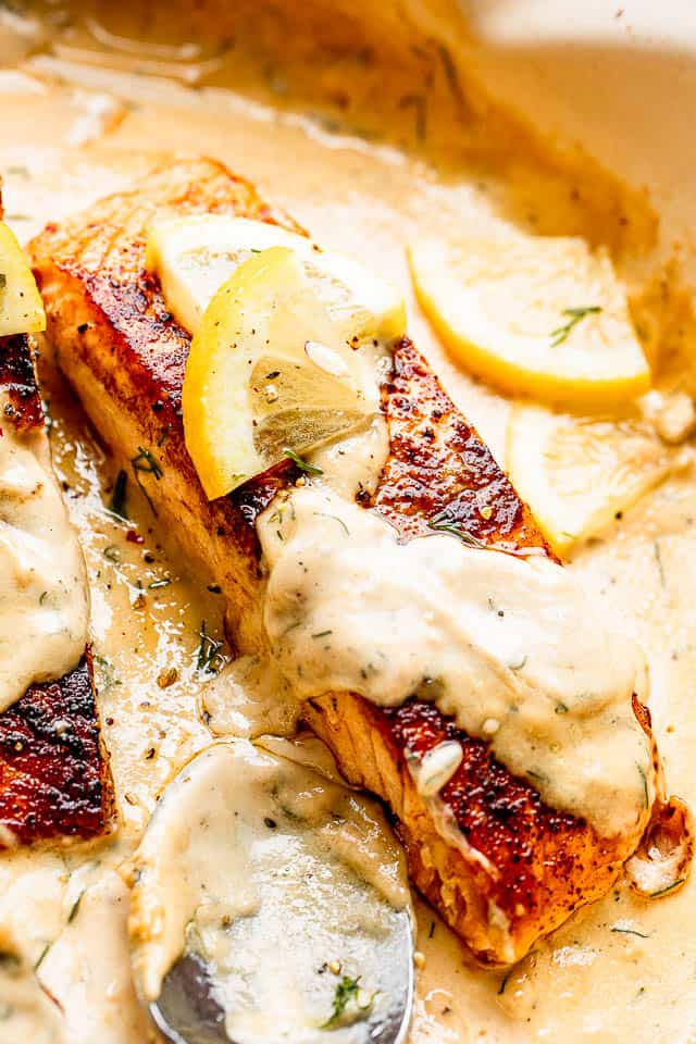 close up of cooked salmon fillet topped with creamy dill sauce and a slice of lemon