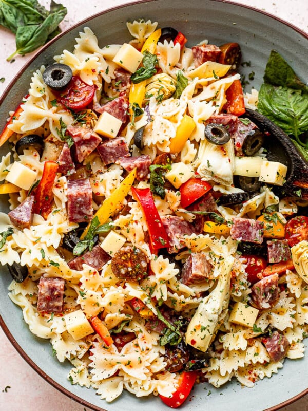 top view of a large blue salad bowl with pasta, olives, cheeses, and salami