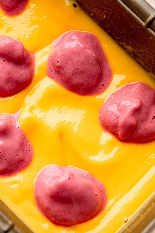 close up shot of a blended mango mixture topped with dollops of blended strawberry mixture