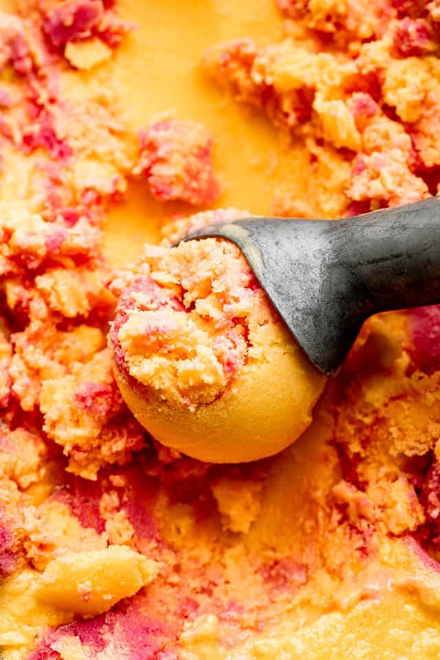 close up shot of mango strawberry frozen yogurt in an ice cream scoop