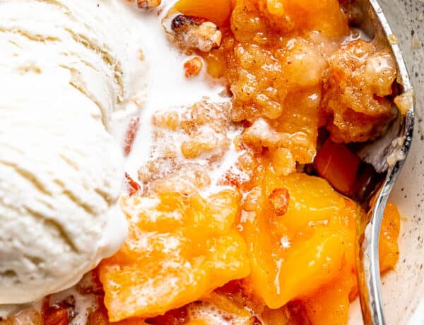 silver spoon inside a white bowl filled with a Peach Dump Cake and a scoop of ice cream