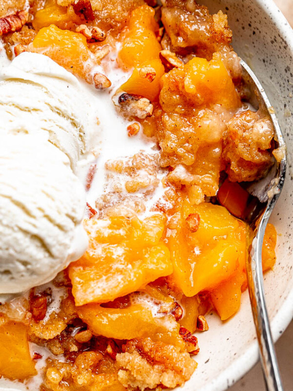 silver spoon inside a white bowl filled with a Peach Dump Cake and a scoop of ice cream