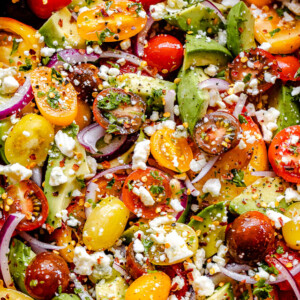 top shot of a wooden salad bowl filled with tomatoes, onions, avocado, and bleu cheese