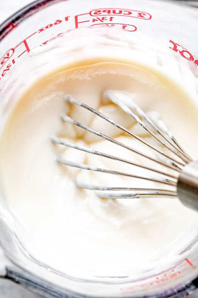 whisking cream cheese frosting in a glass measuring cup