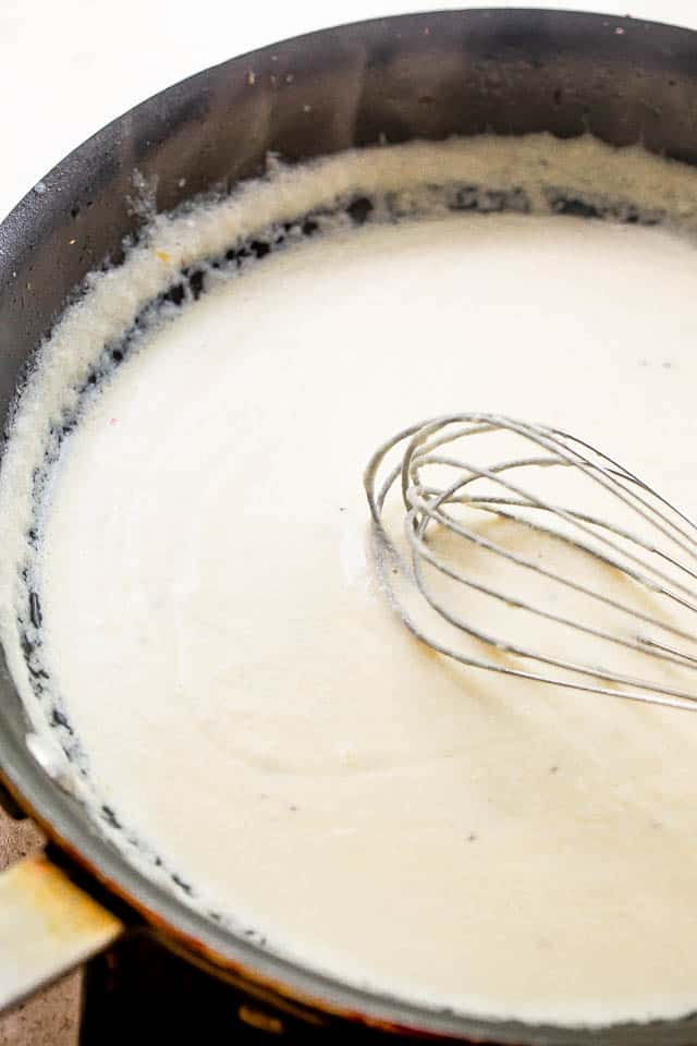 whisking cream cheese sauce in a black skillet