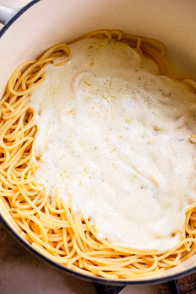 white dutch oven with spaghetti and white cream sauce on top