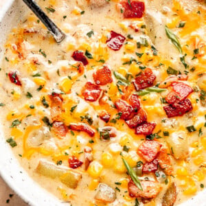 silver spoon inside corn chowder soup in a bowl topped with bacon, green onions, and parsley