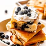 side shot of stacked sheet pan pancakes topped with whipped cream and blueberries