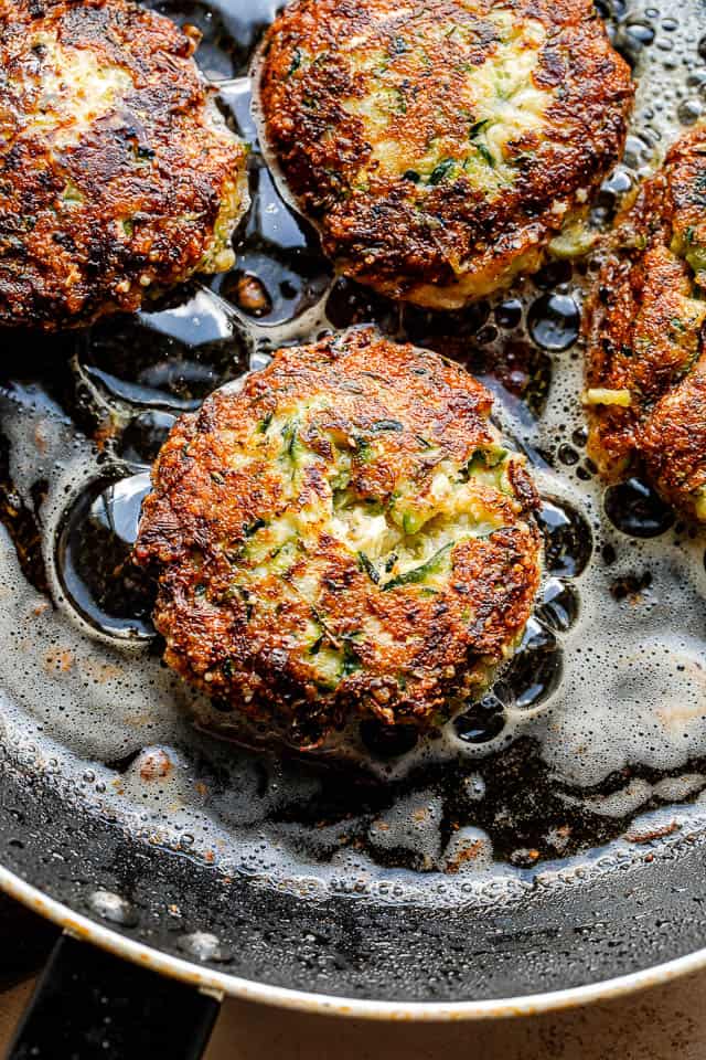 frying zucchini patties in a black colored skillet