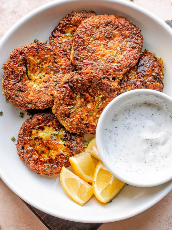 top shot of zucchini cakes in a white bowl with lemon wedges and dip