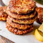 stacked zucchini patties with lemon wedges next to them and yogurt dip behind