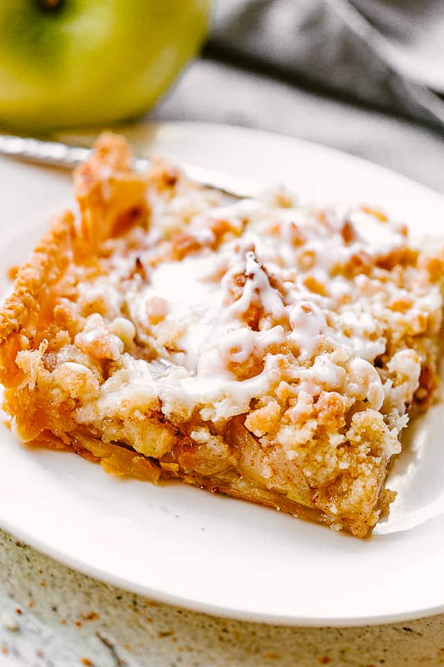 slice of apple slab pie on a white dessert plate set next to a green apple.