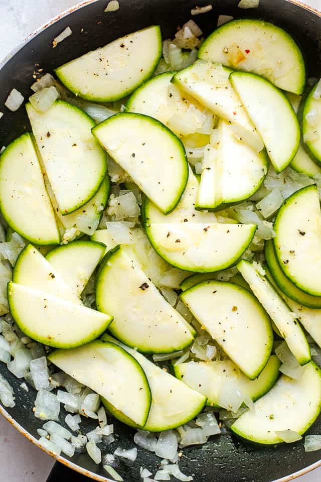 frying zucchini slices and diced onion in a black skillet