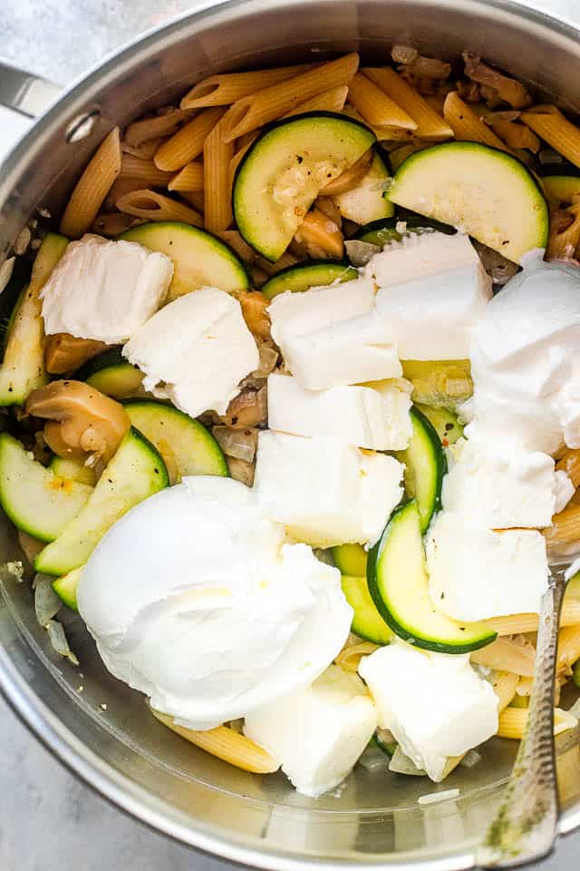 overhead shot of a silver pot filled with pasta, zucchini slices, and cubed cream cheese