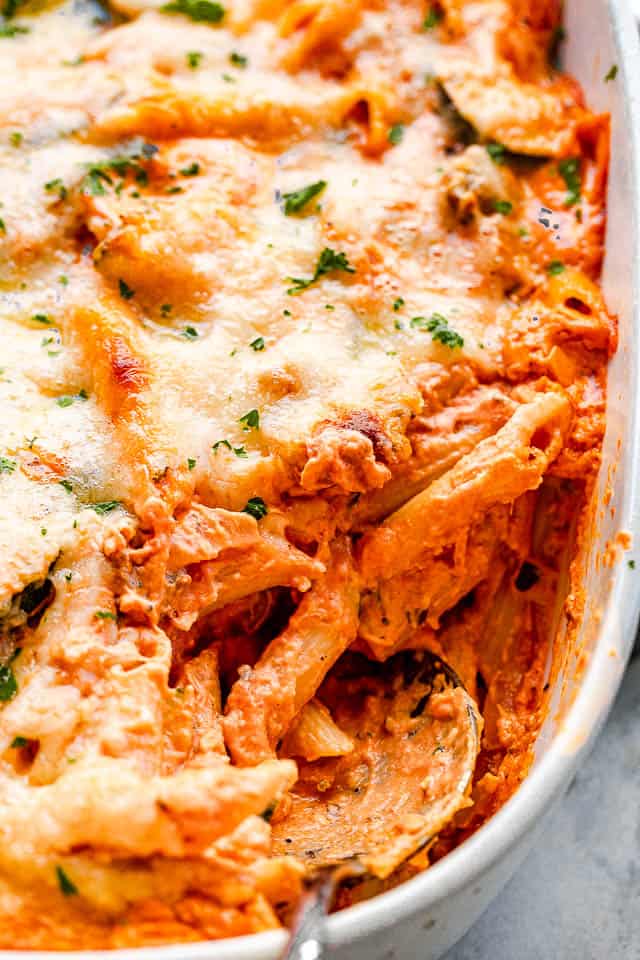 side view of a cheesy pasta in a baking dish with a serving spoon pulling out the food