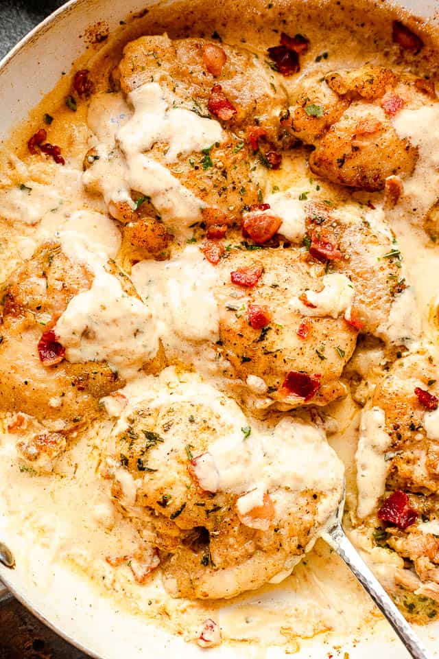 top view of cooked cream sauce chicken thighs in a white skillet with a silver serving spoon picking up the food