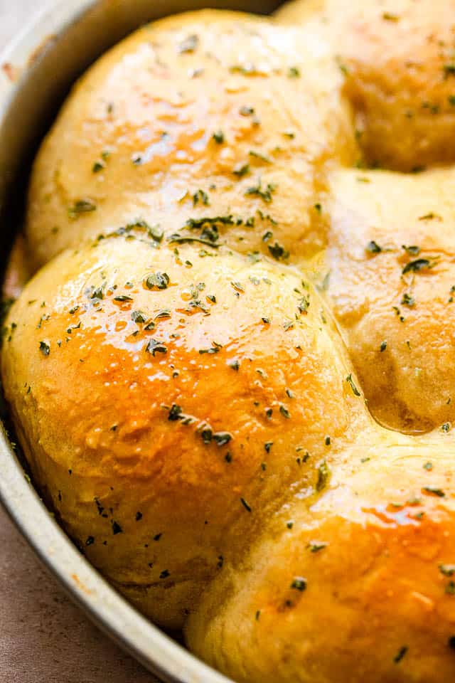 side view close up shot of baked dinner rolls sprinkled with herbs and set in a pan