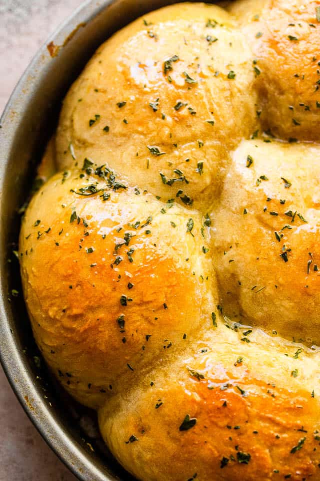 overhead close up shot of baked dinner rolls sprinkled with herbs and set in a pan