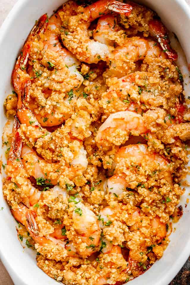 overhead shot of arranged shrimp in a white oval dish and topped with garlic butter and breadcrumbs mixture