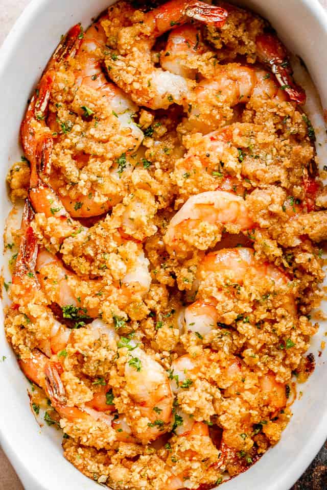 overhead shot of arranged shrimp in a white oval dish and topped with garlic butter and breadcrumbs mixture.