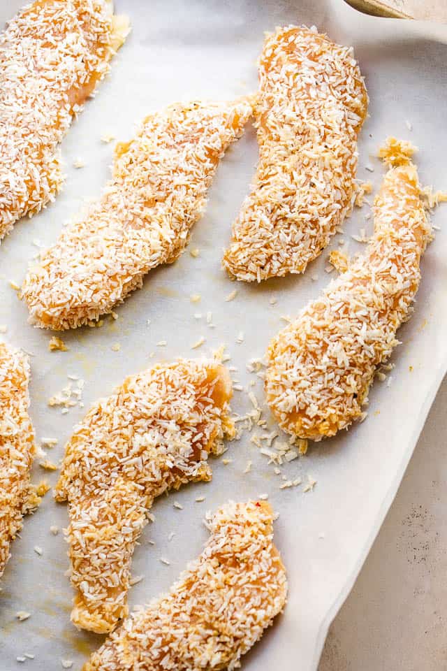 overhead shot of raw coconut covered chicken tenders on a baking sheet