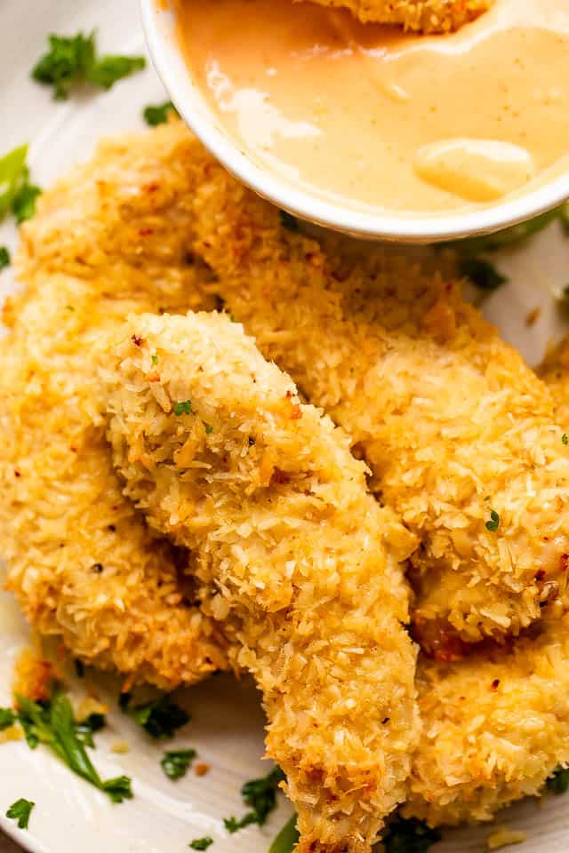 four chicken tenders with dipping sauce served on a plate