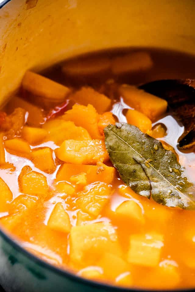 Diced Butternut squash simmering in broth, with a bay leaf set on top of the liquid.