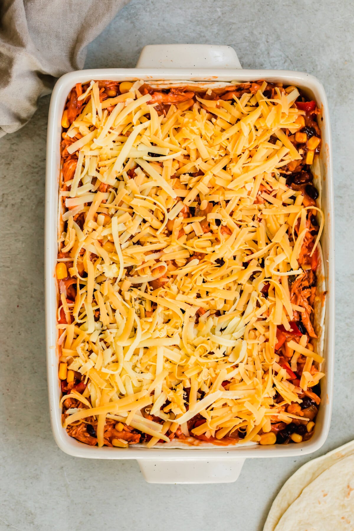 A Chicken Enchilada Casserole in a White Pan Topped with Shredded Cheese