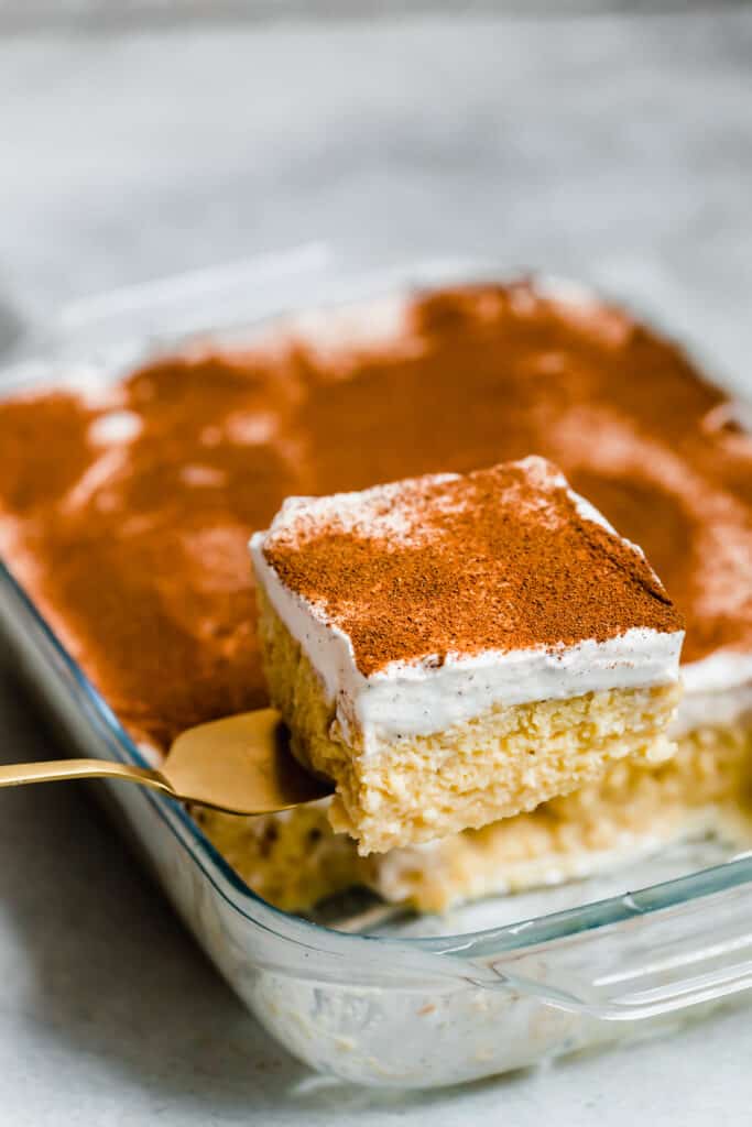 A Square of Tres Leches Cake Being Lifted From the Glass Pan with a Serving Spatula