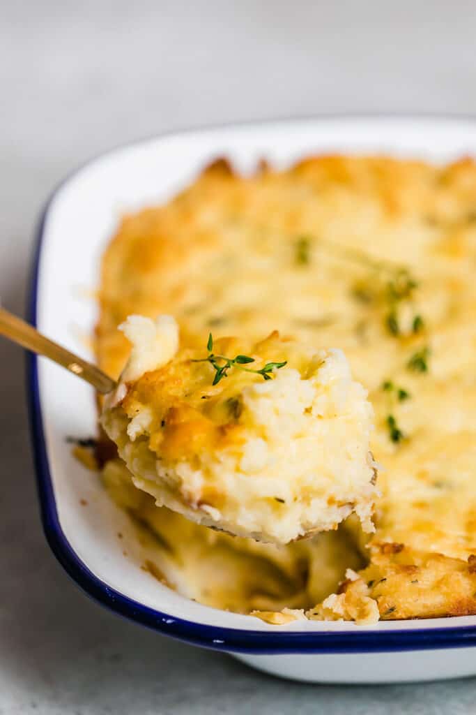 close up side shot of scooping out mashed potatoes from baking dish