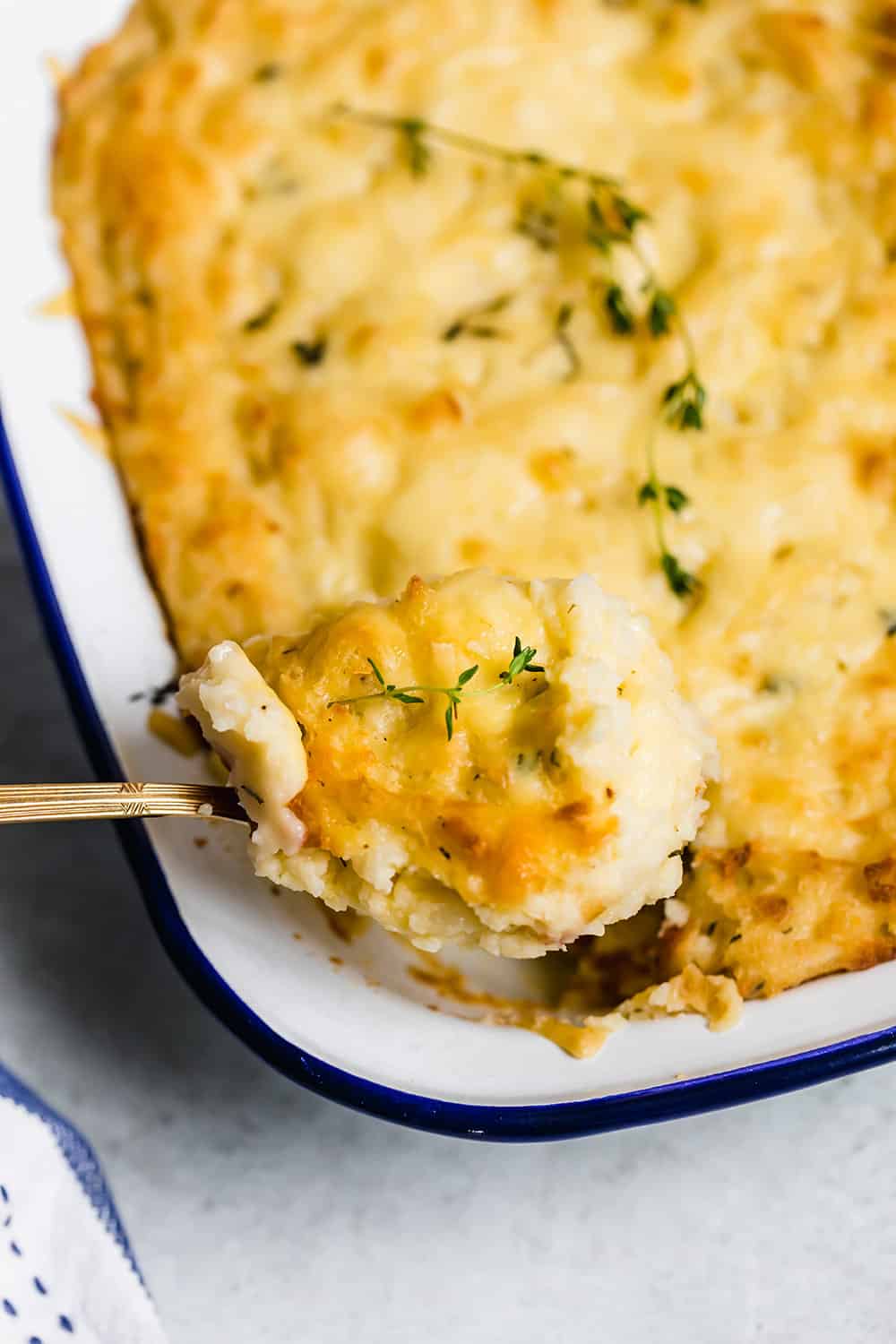 A spoon scooping baked mashed potatoes out of a casserole dish.