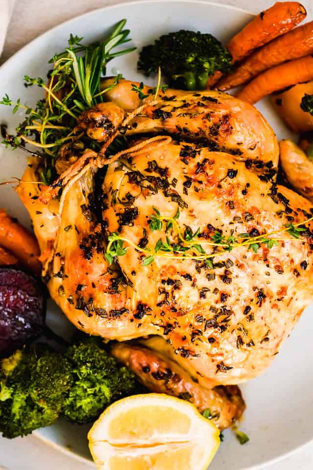 close up overhead shot of a whole chicken on a white serving platter with vegetables