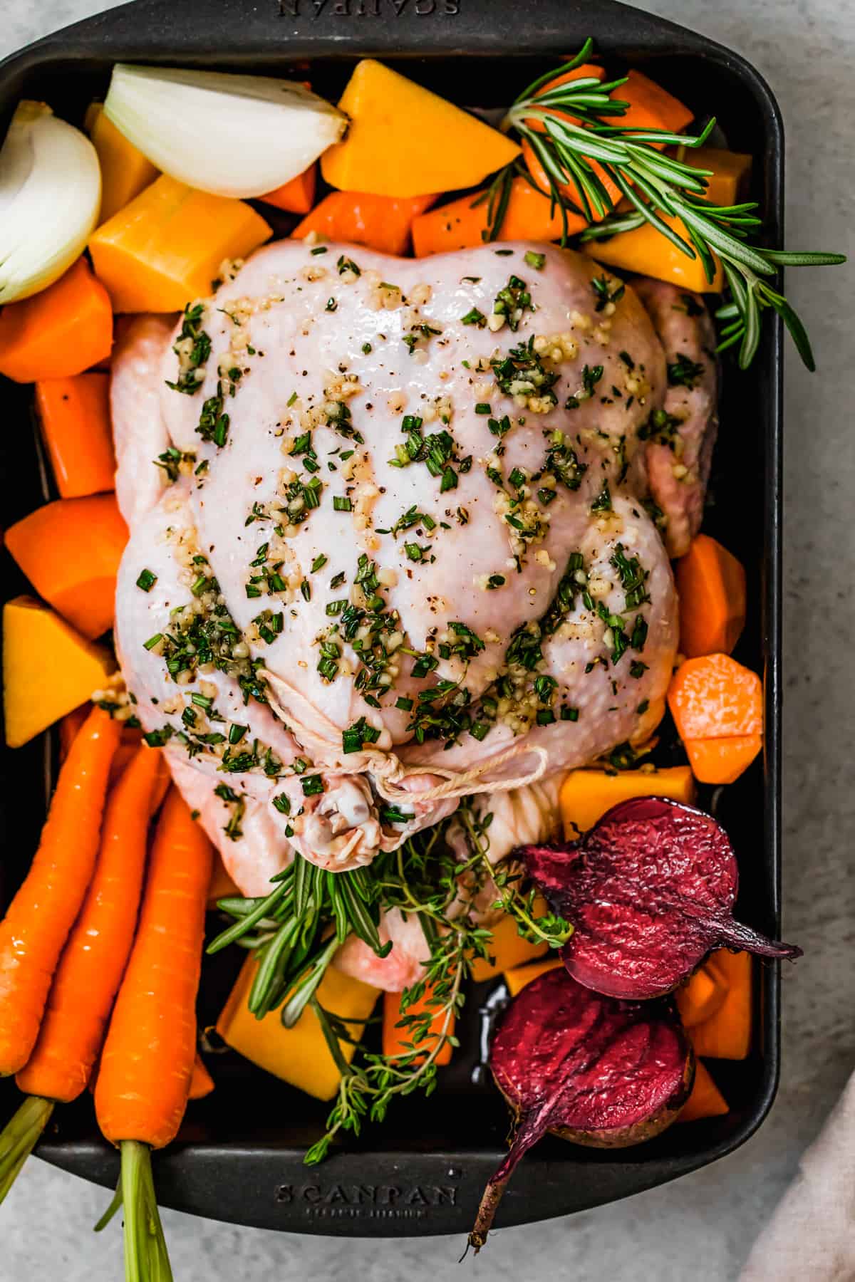 Whole raw broiler chicken in a baking pan with root vegetables.