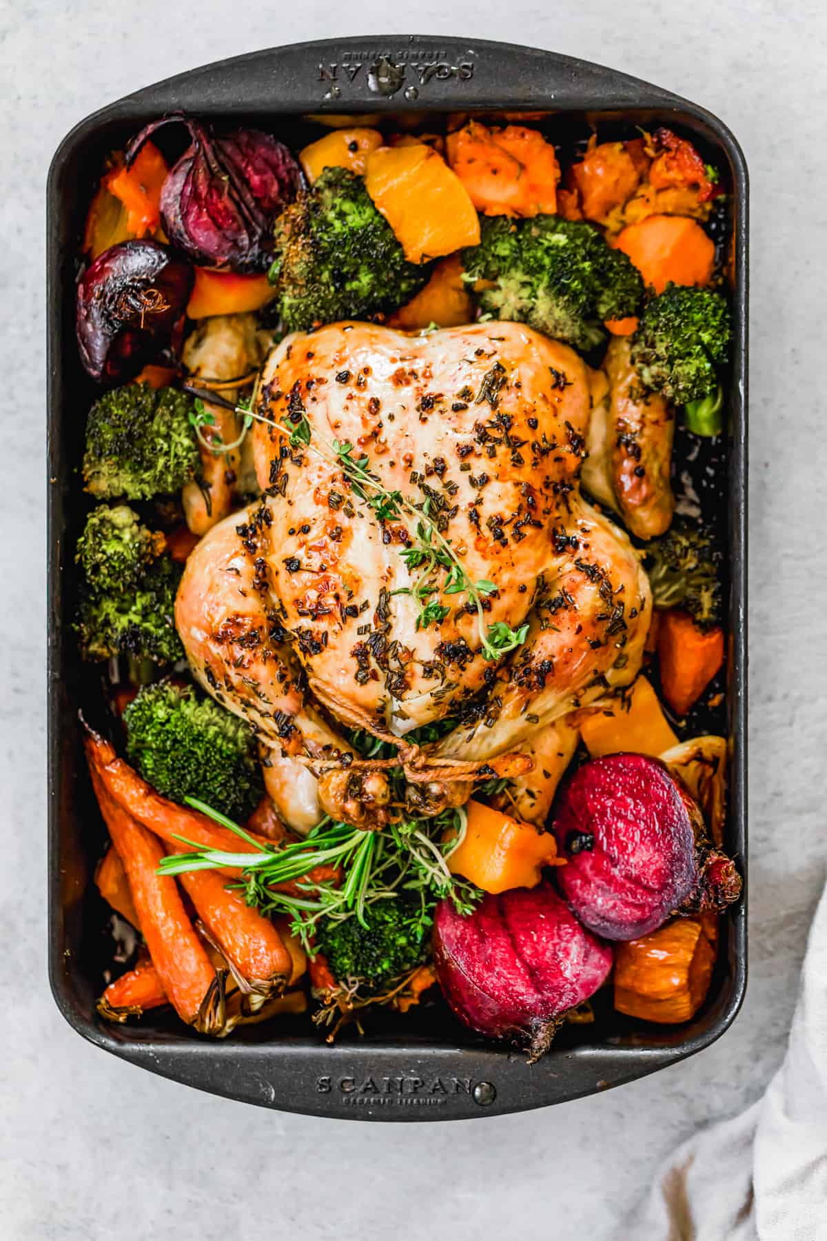 Whole roast chicken with fall vegetables on a sheet pan.