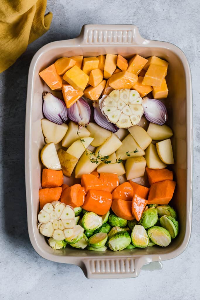 Chopped root vegetables in a roasting pan with oil and thyme.