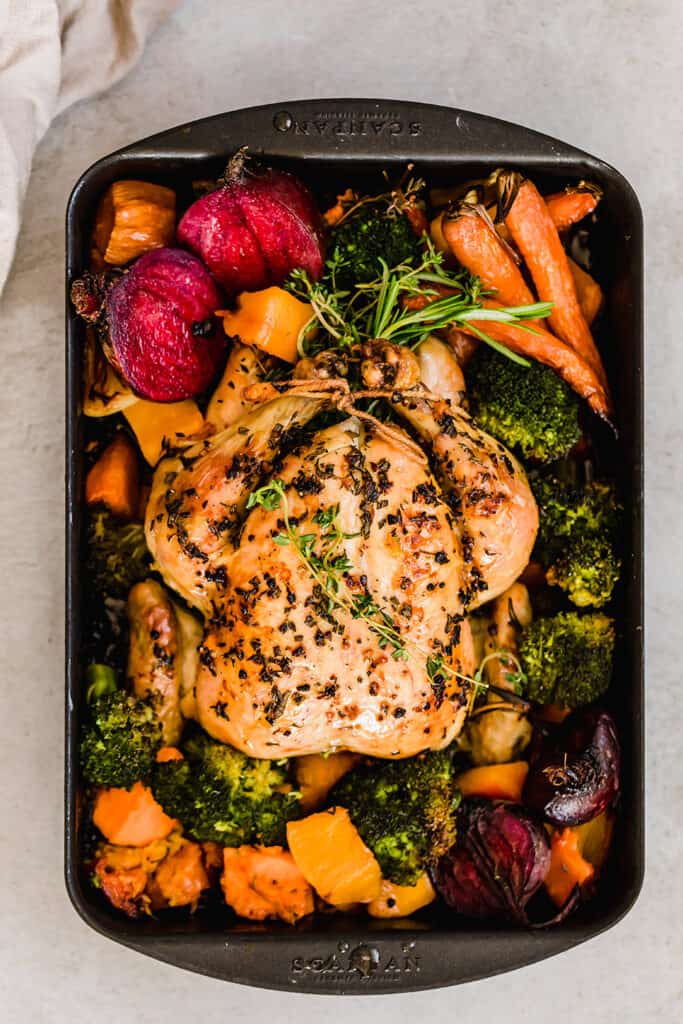 overhead wide shot of whole chicken roasted with fall vegetables in a roasting pan