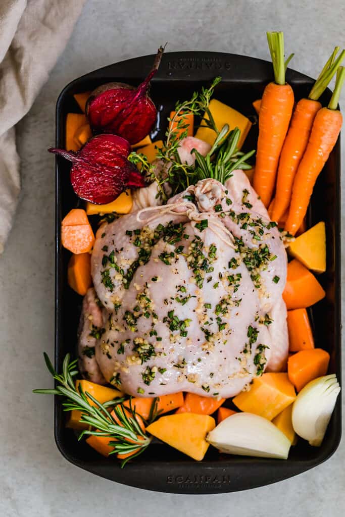 wide shot of raw whole chicken set over veggies in a roasting pan 