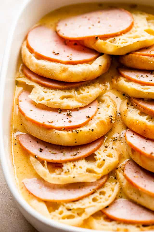 english muffins and canadian bacon layered in a white baking dish.