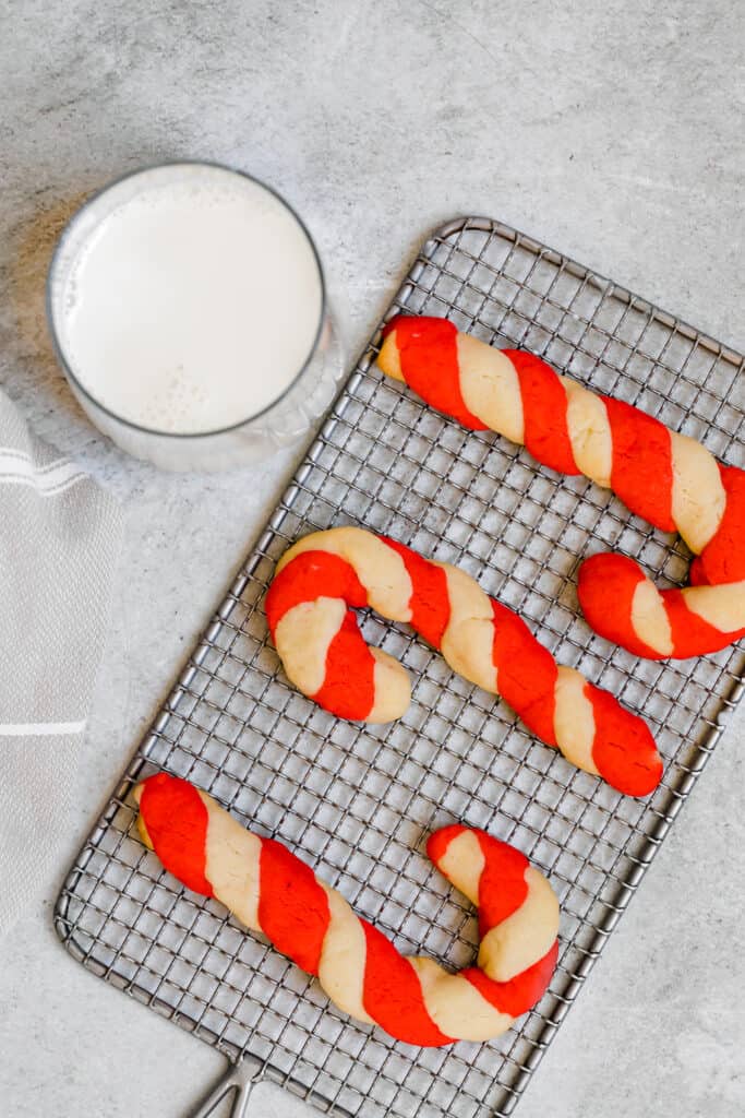 Three Candy Cane Cookies on a Cooling Rack Beside a Glass of Milk