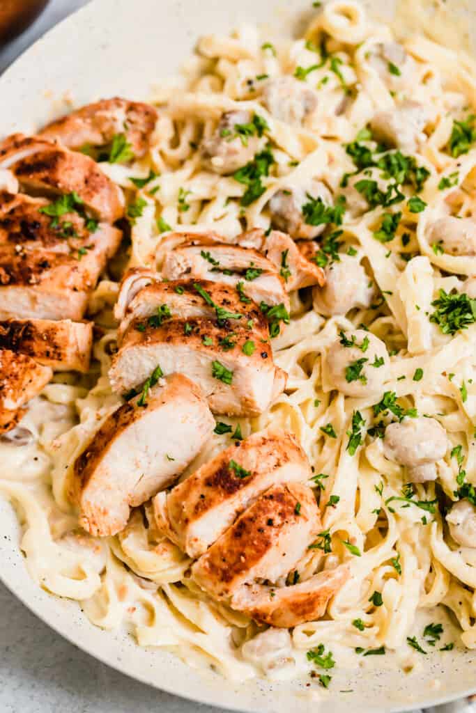 A Close-Up Shot of Sliced Chicken Breasts and Fettuccine Pasta with Alfredo Sauce