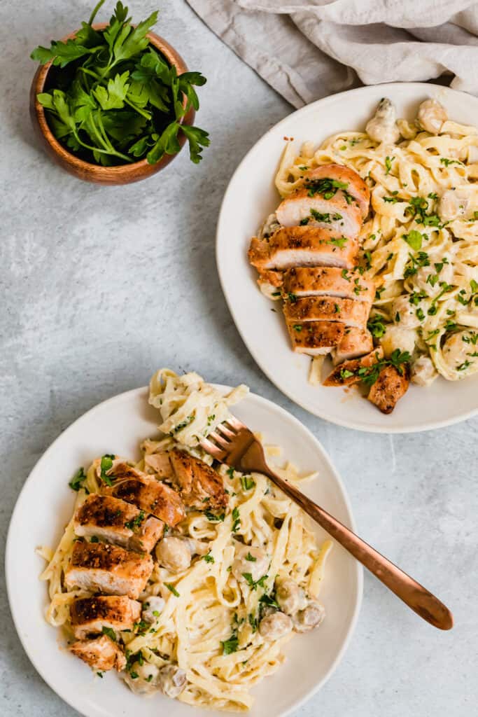 Two Bowls of Chicken Fettuccine Alfredo Next to a Small Container of Parsley Leaves