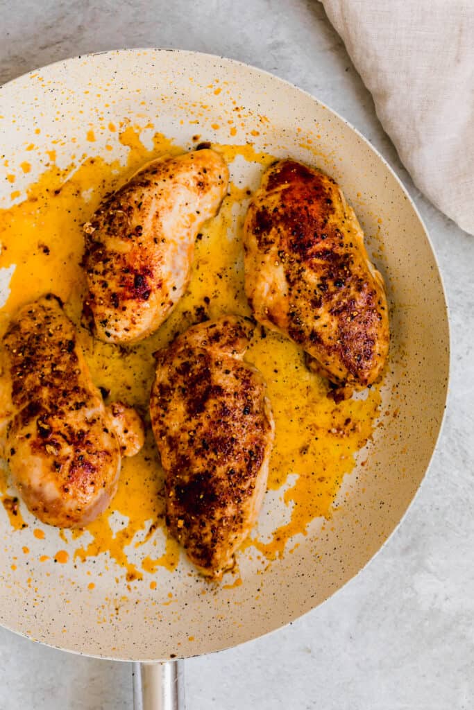 Four Cooked Chicken Breasts in a Black and White Skillet