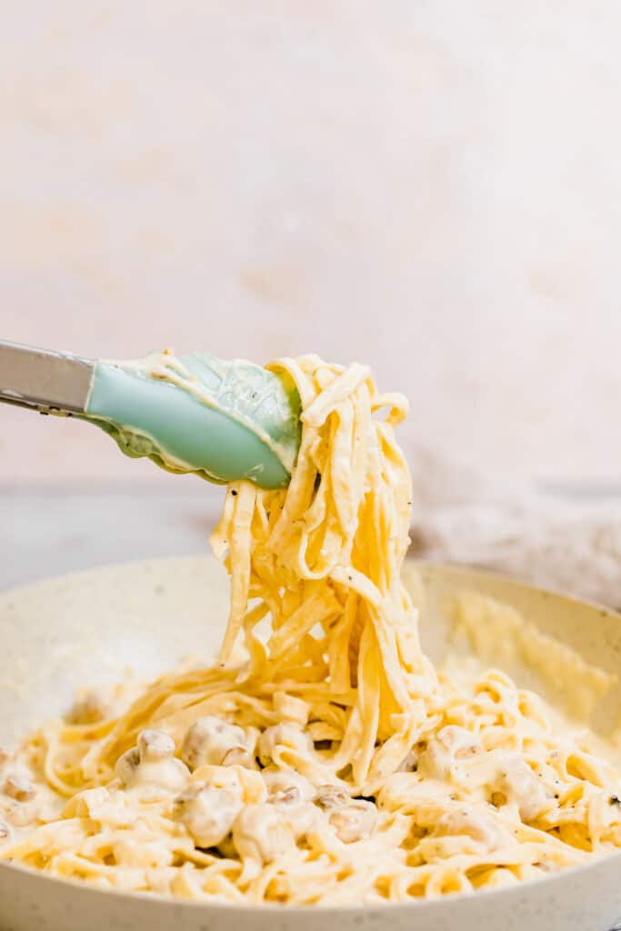 A Pair of Tongs Grabbing a Bunch of Fettuccine Noodles Covered in Alfredo