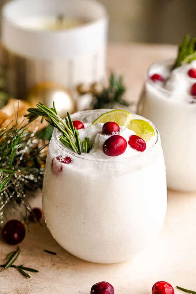 drinking glass filled with margaritas and garnished with lime slices, rosemary sprigs, and cranberries