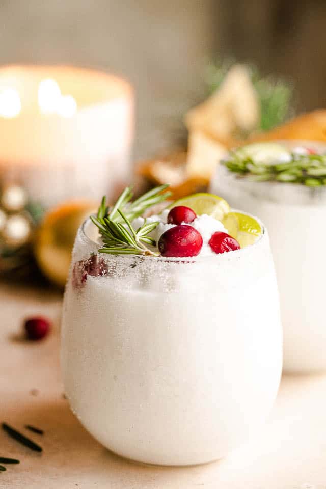 drinking glass filled with margaritas and garnished with lime slices, rosemary sprigs, and cranberries