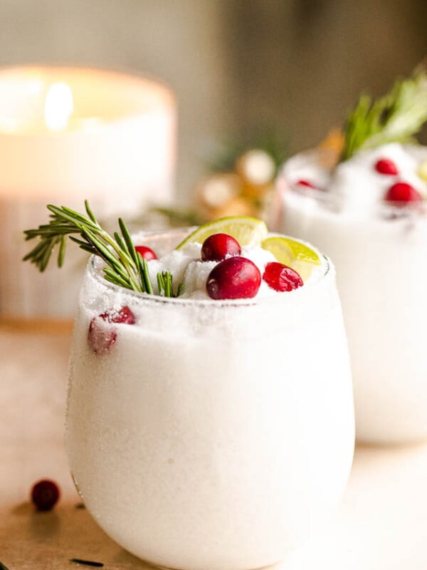 drinking glasses filled with white frozen margaritas and garnished with lime slices, rosemary sprigs, and cranberries