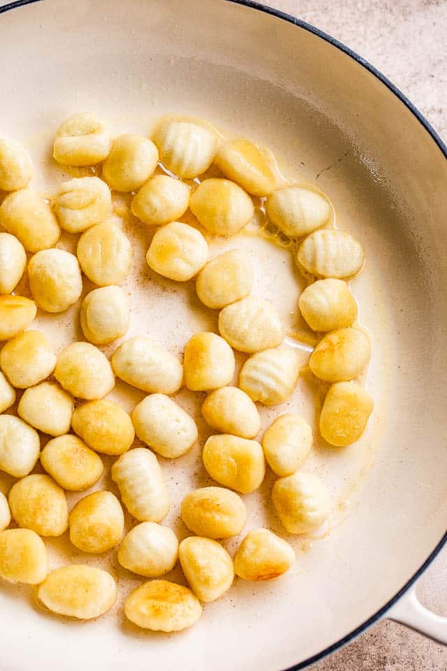 frying gnocchi in a white skillet