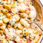 spooning out creamy gnocchi from a casserole dish