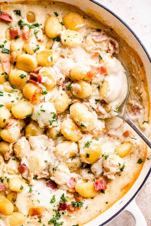 spooning out creamy gnocchi from a casserole dish