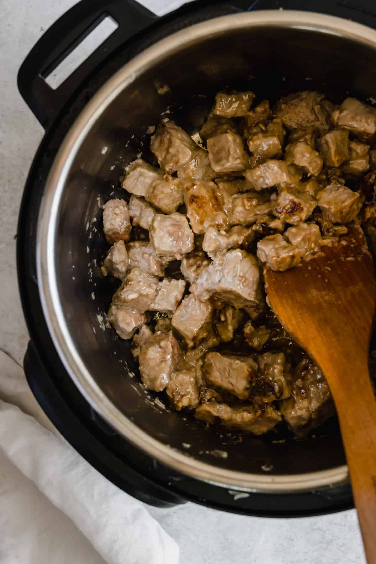 Beef Being Stirred Around in the Instant Pot by a Wooden Spoon